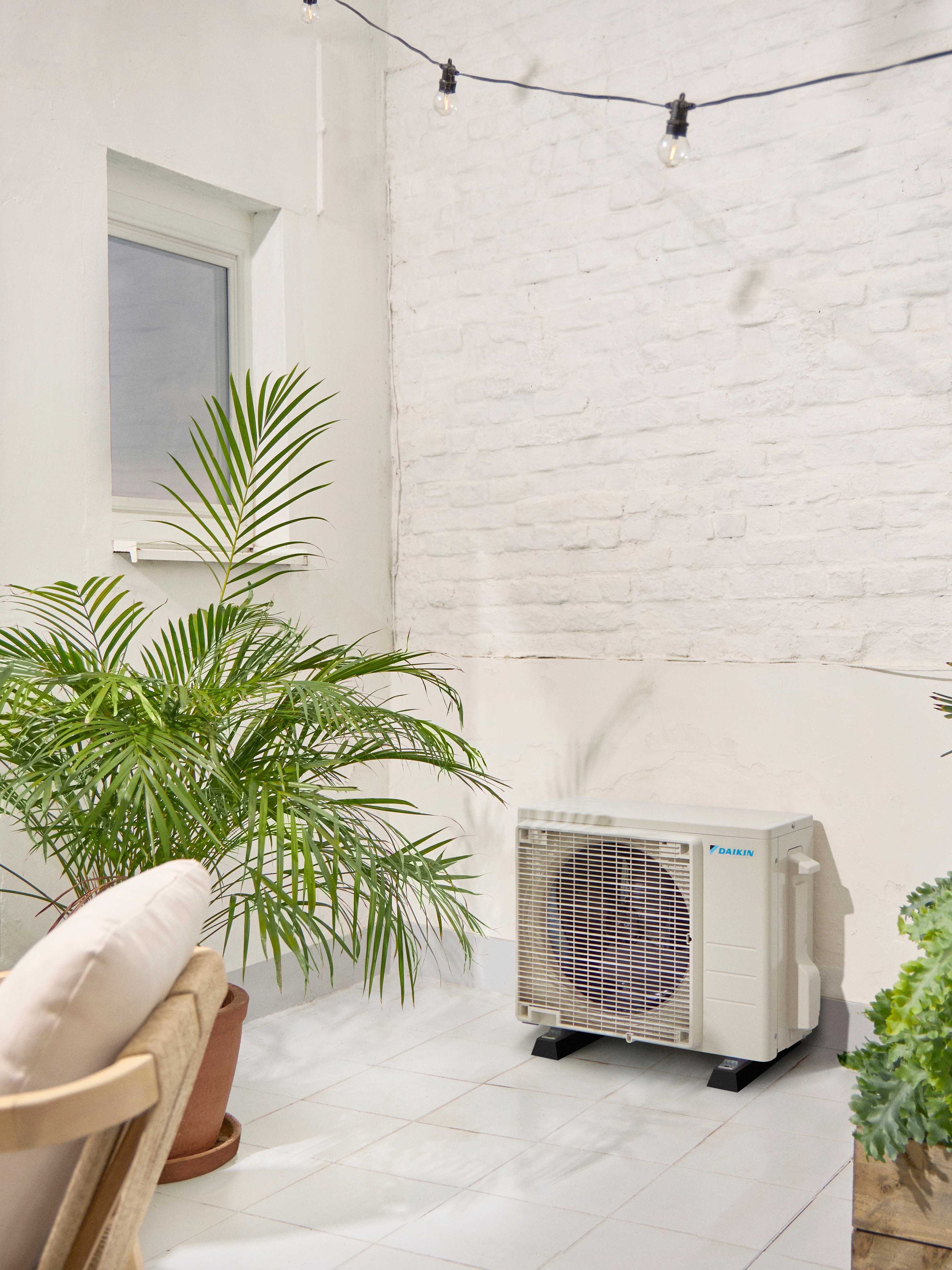 Utomhusenhet från Daikin på en vit terrass med en växt
