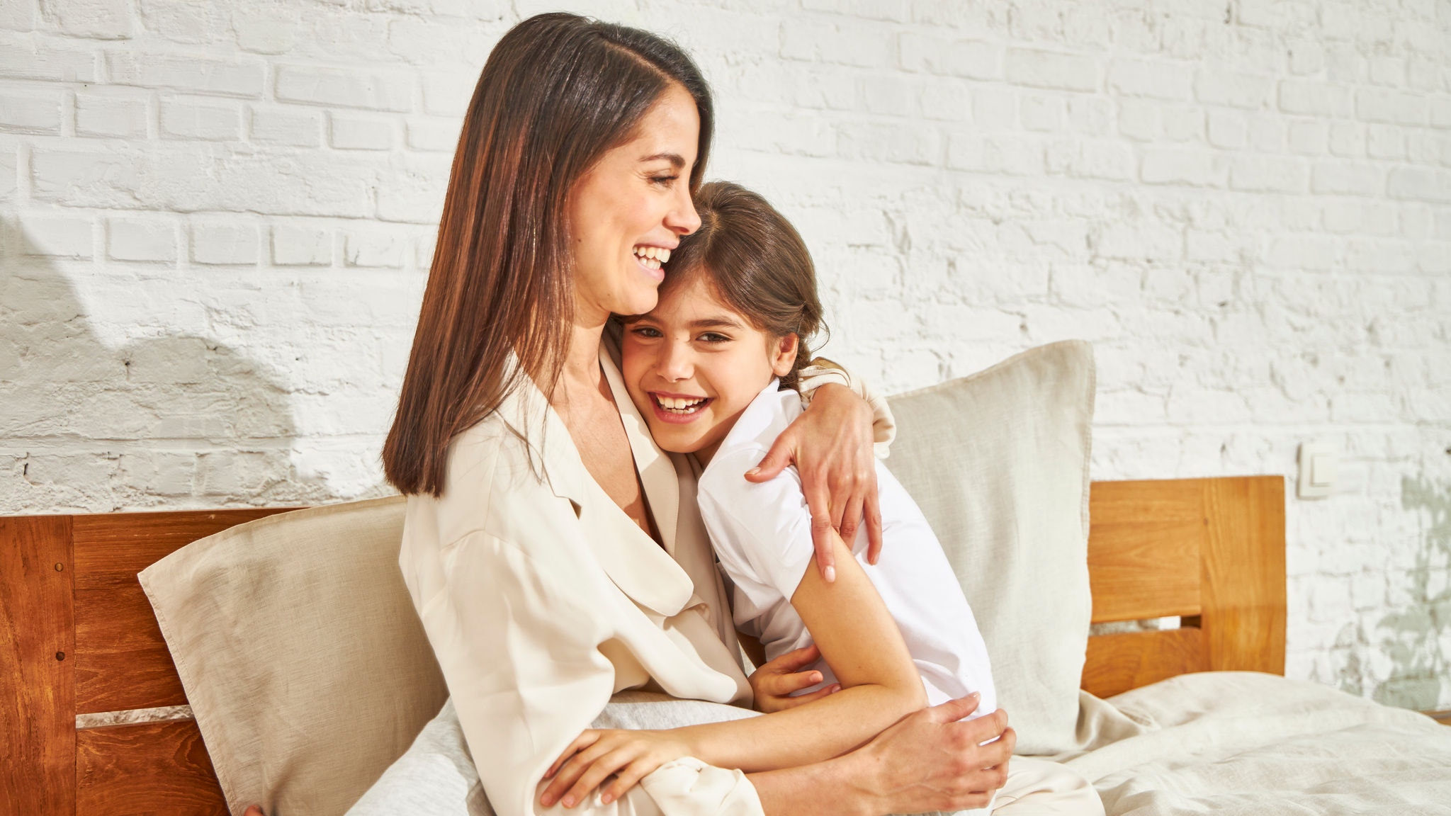 En mor och sin lilla dotter ler och kramas medan de sitter på en säng