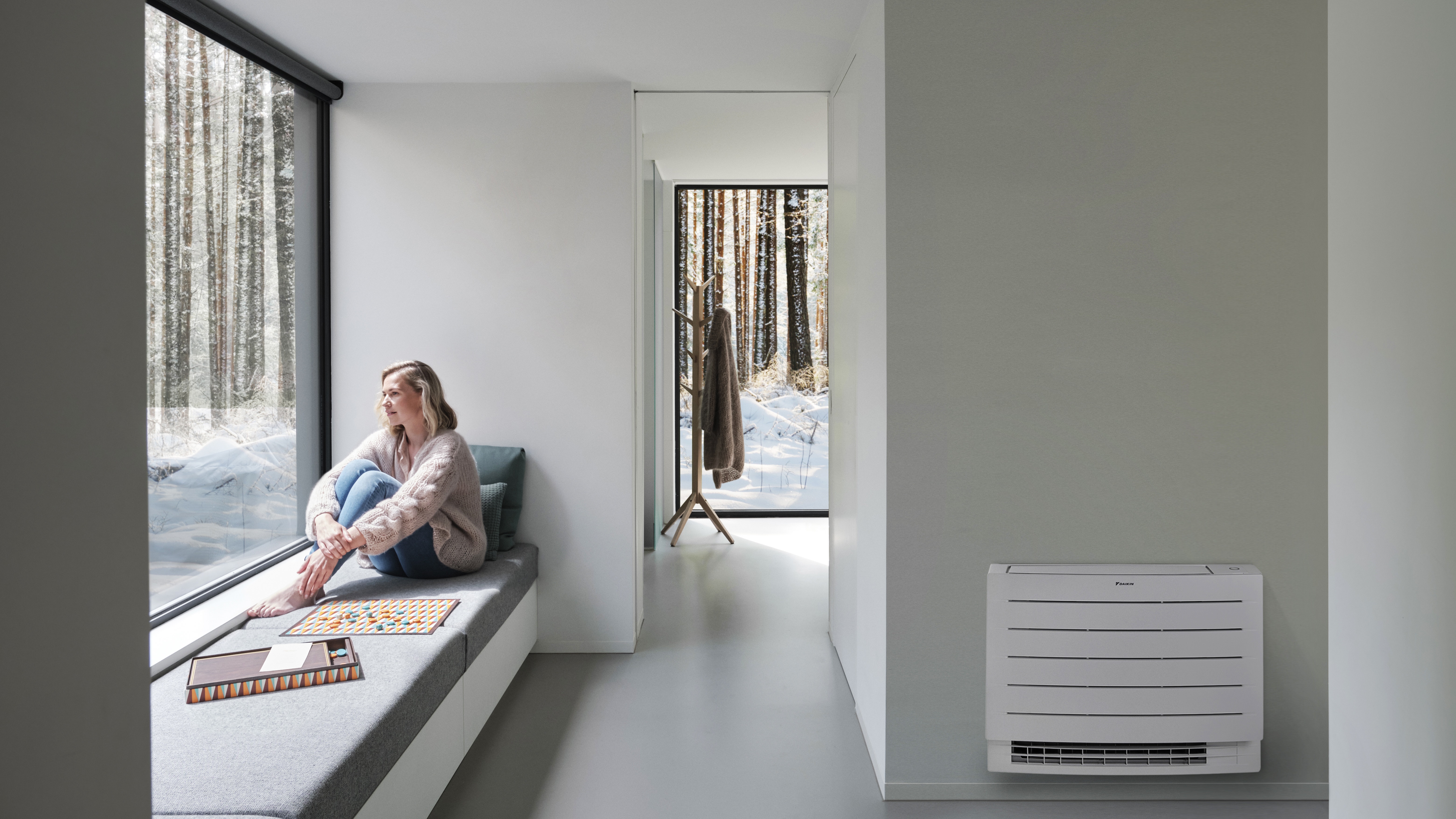 En kvinna som tittar på det vita snötäcket utanför sitt hus, och njuter av ett uppvärmt hem tack vare en Perfera golvmonterad luftvärmepump