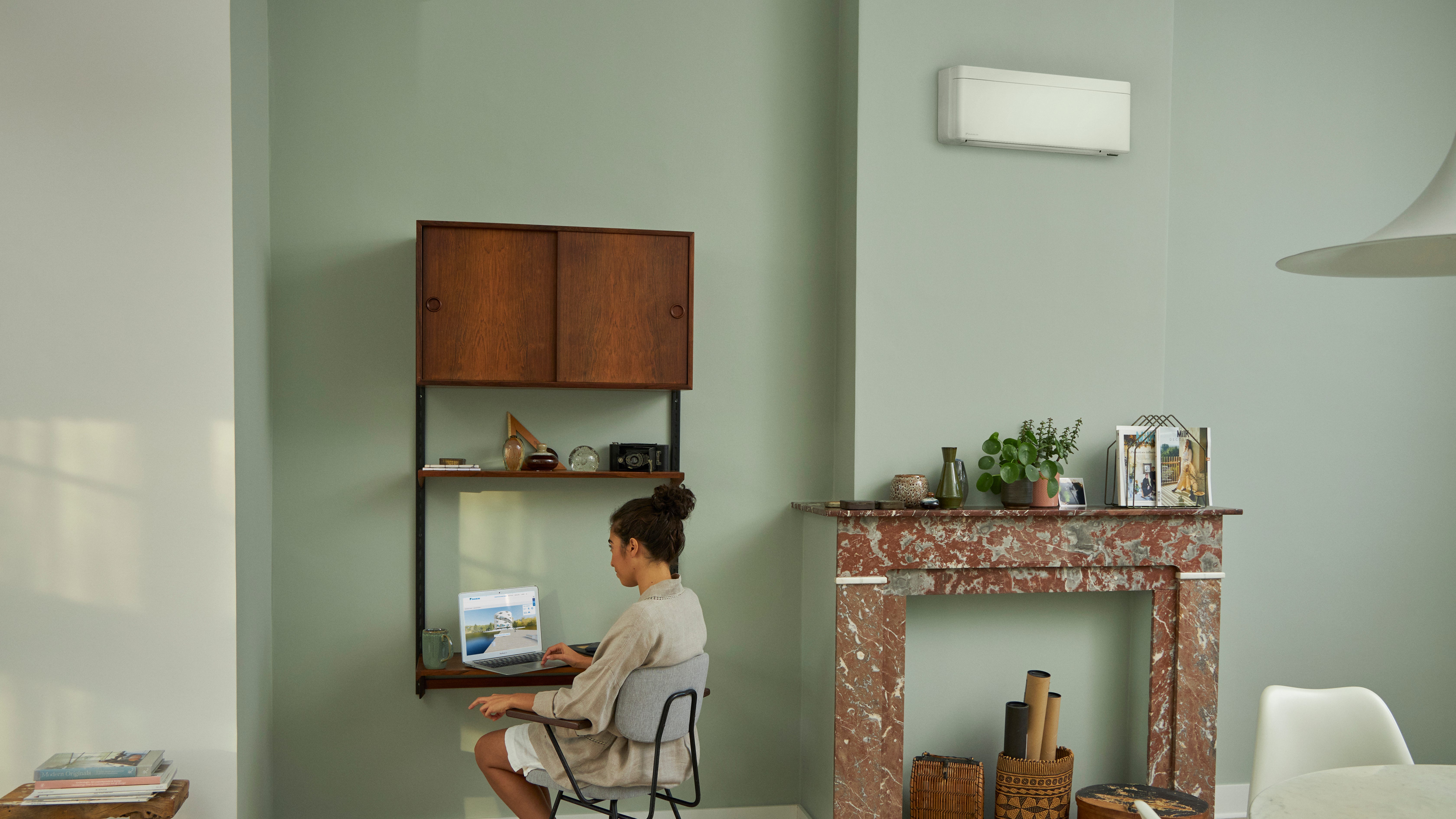 En kvinna som besöker Daikin Virtual Experience Center i sin bärbara dator, sittande vid sitt lilla skrivbord i ett vackert inrett vardagsrum